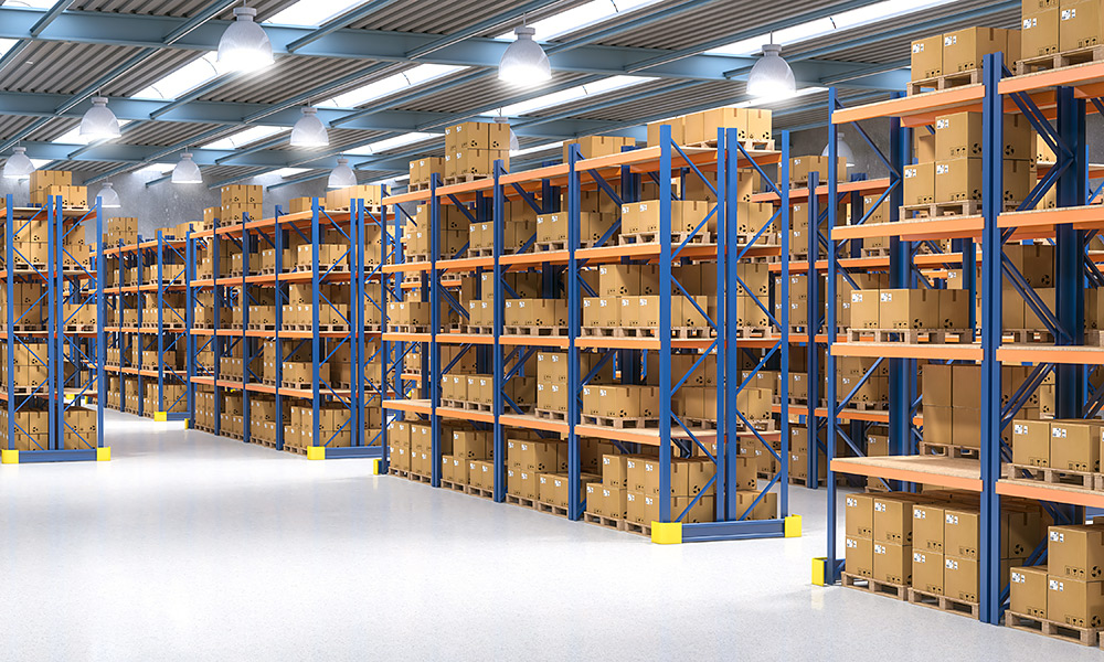 A large, well-organized warehouse with tall blue and orange shelving racks fully stocked with cardboard boxes on wooden pallets.