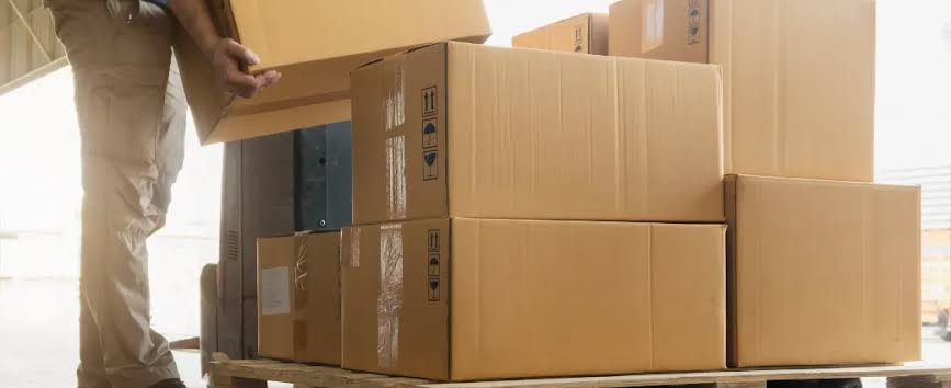 A worker in a warehouse stacking cardboard boxes onto a pallet, representing the process of multiple supplier consolidation for shipping.